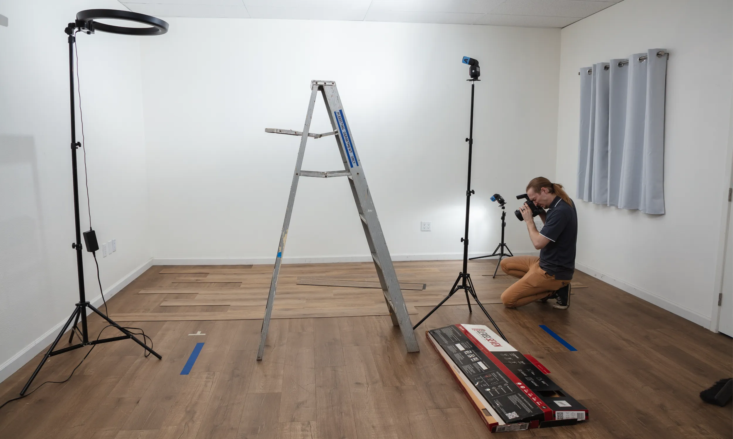A view of a small room with ladder, lighting, plank boxes, and Chris taking photos of the installed floor